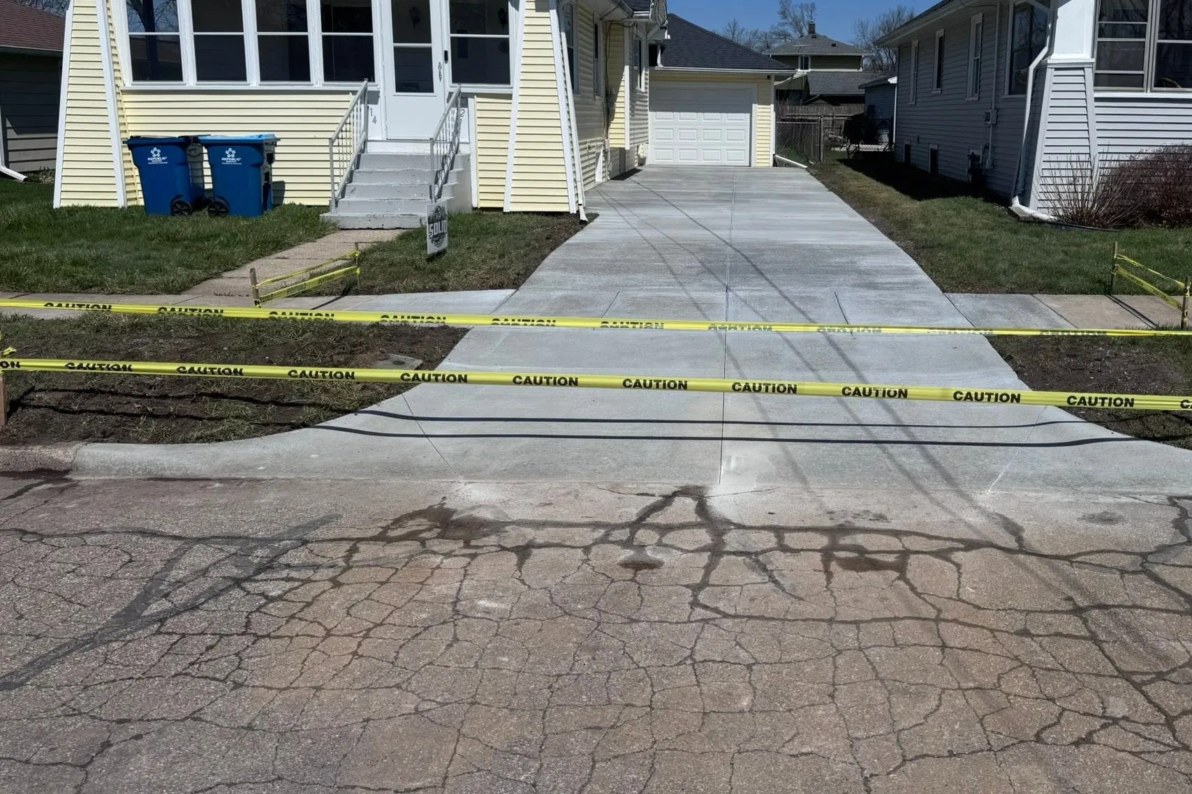 The same driveway after the work: one continuous poured concrete driveway running from the street to the garage, still taped off to cure.