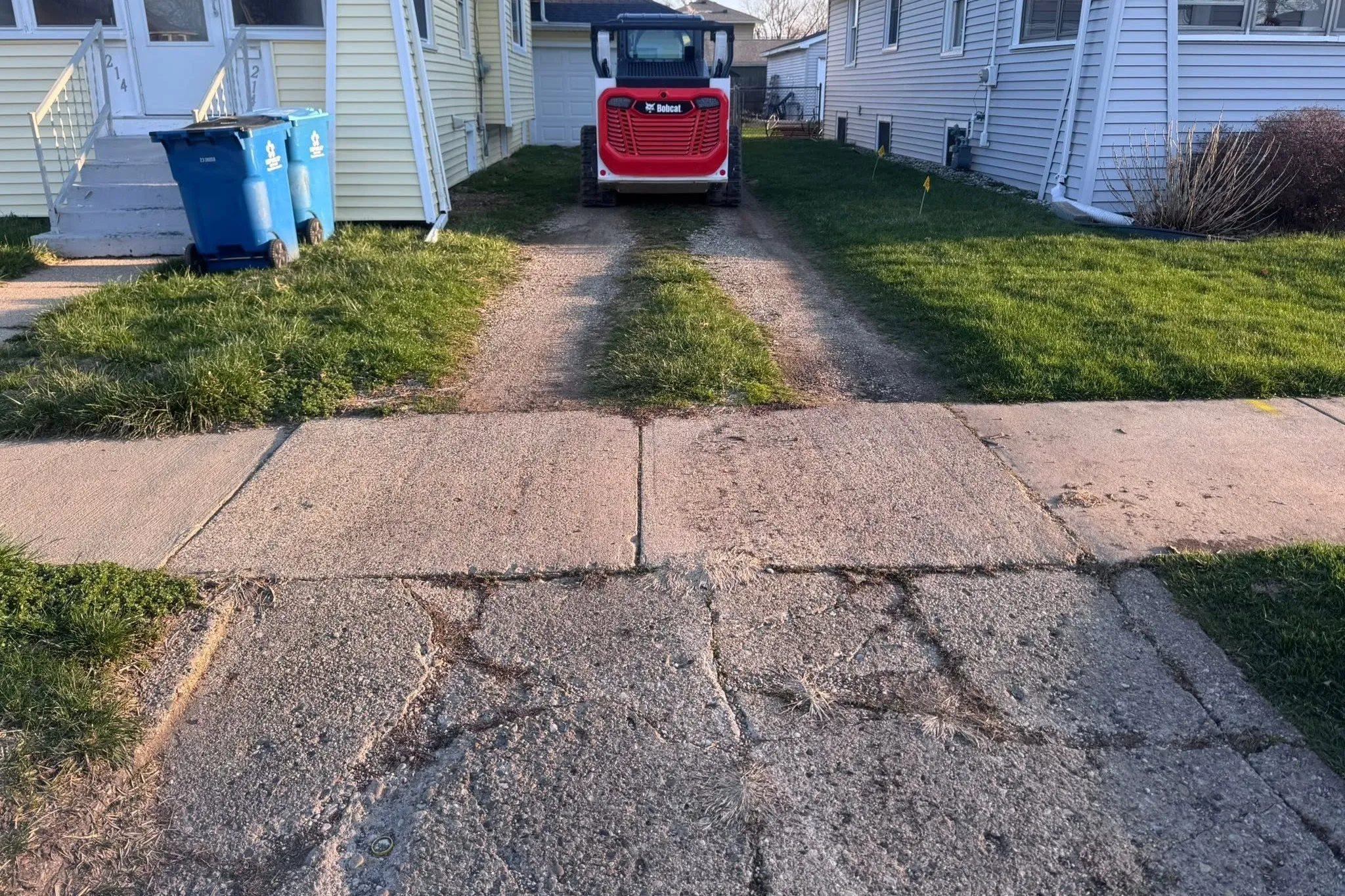 A residential driveway before the work: cracked, broken concrete at the street and a worn gravel two track running back to the garage.