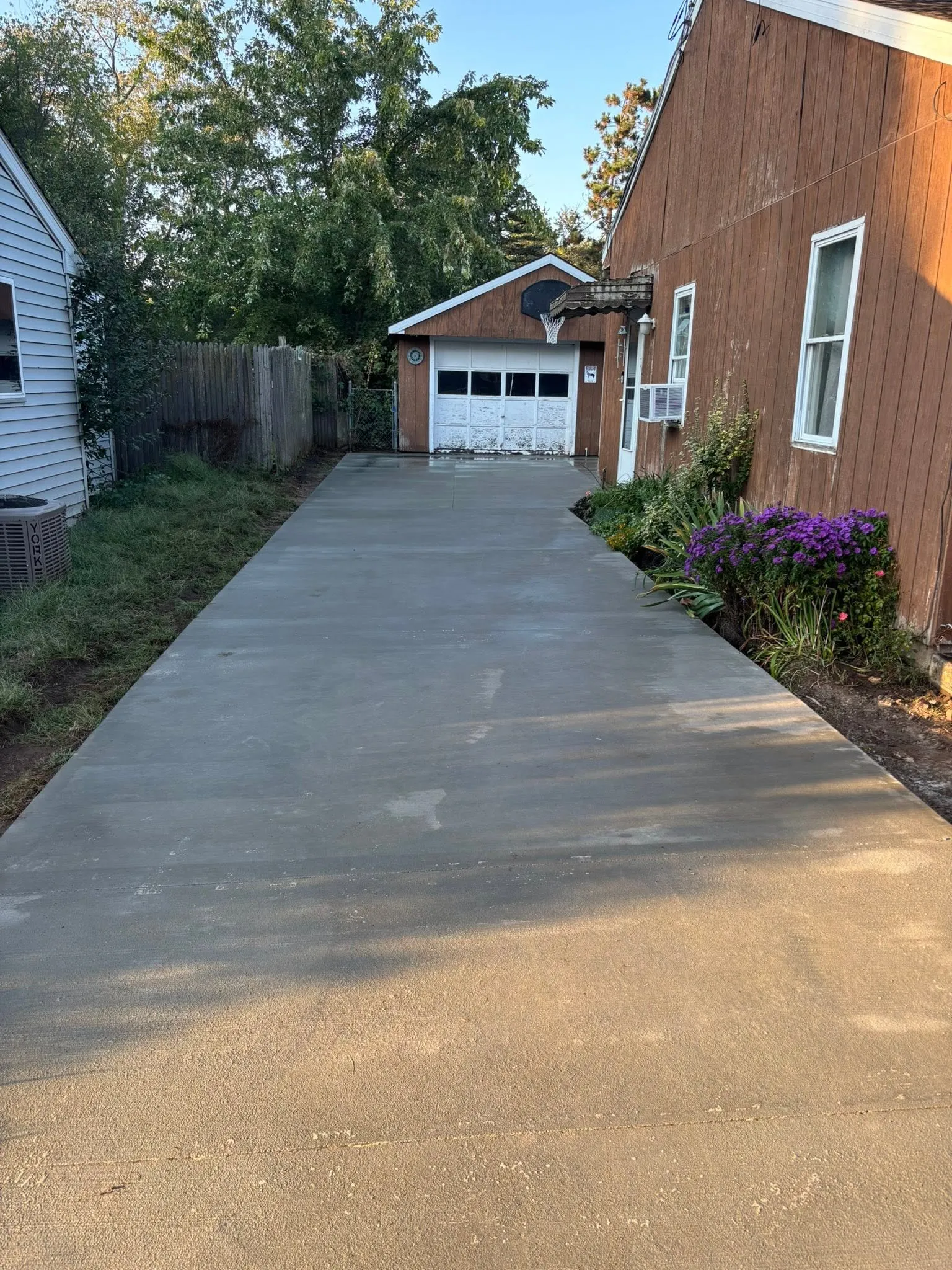 A freshly poured concrete driveway at golden hour, running between the house and a garage with a basketball hoop.