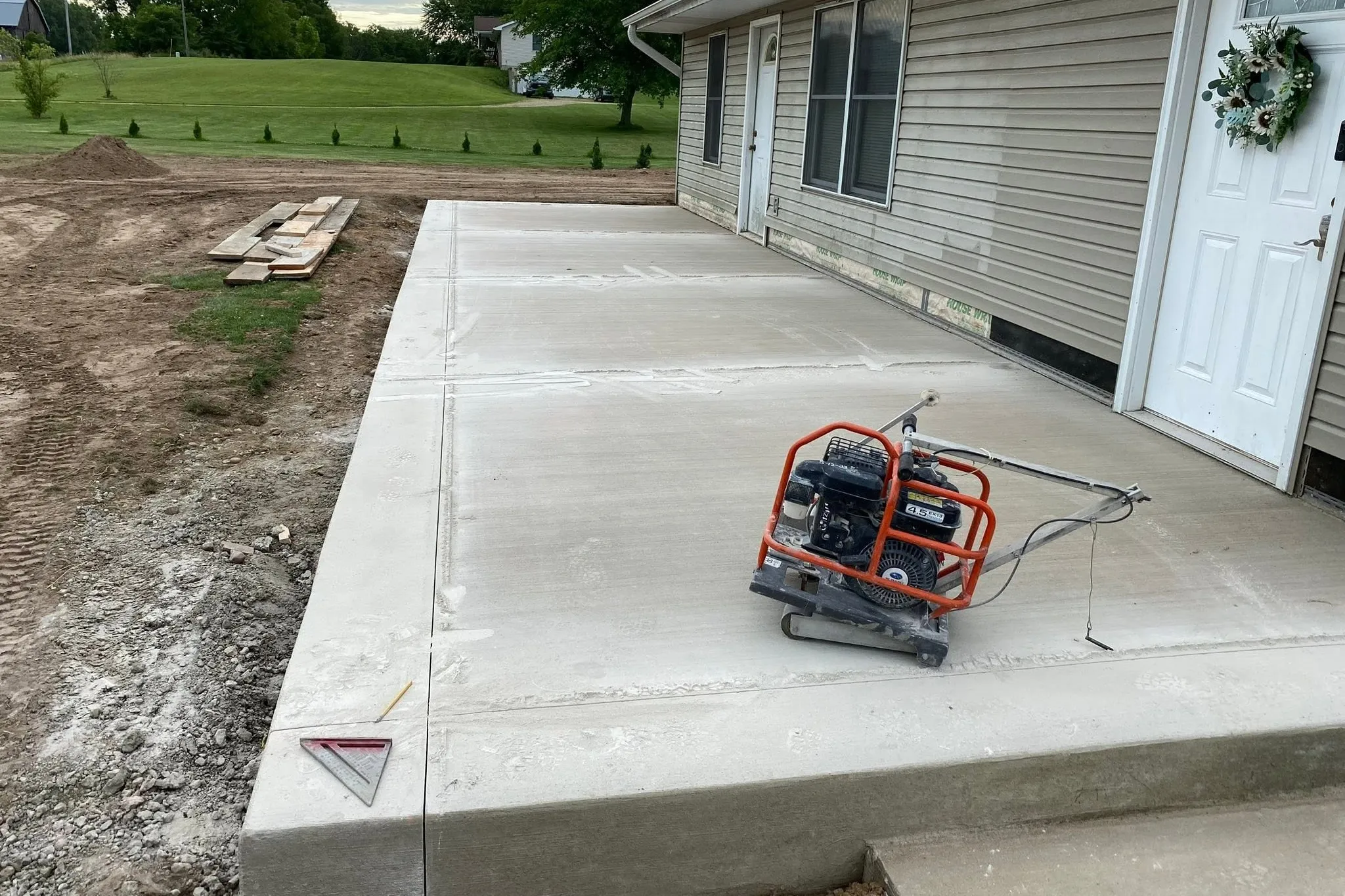 A freshly poured and finished concrete patio slab running the length of a house, with the forms just stripped.