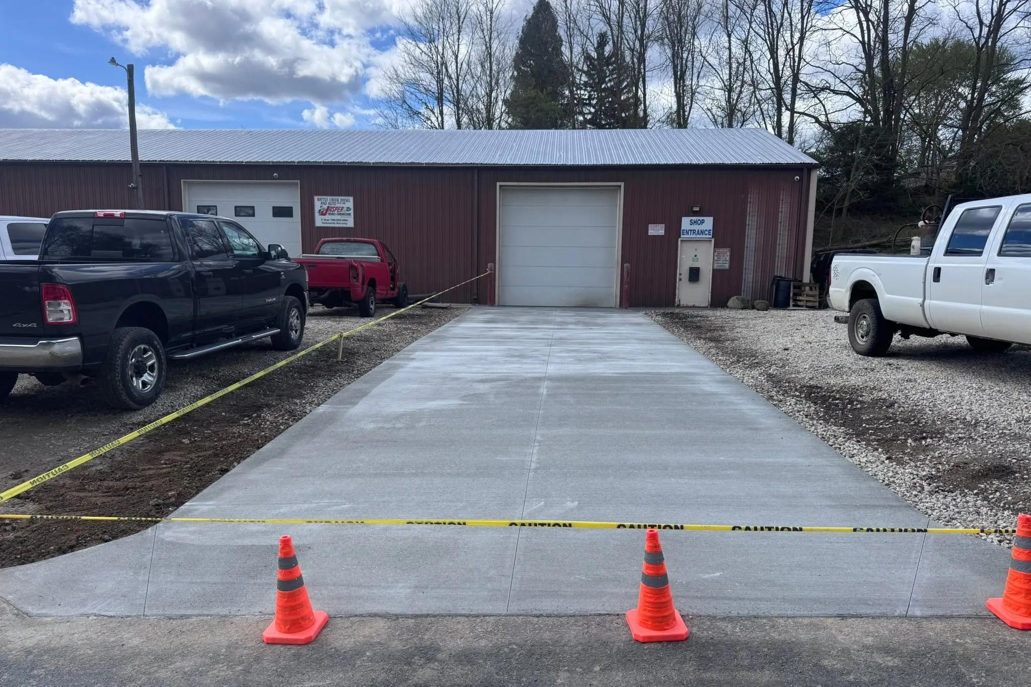The same shop approach after the work: a wide concrete pad running straight into the overhead door, coned off to cure.